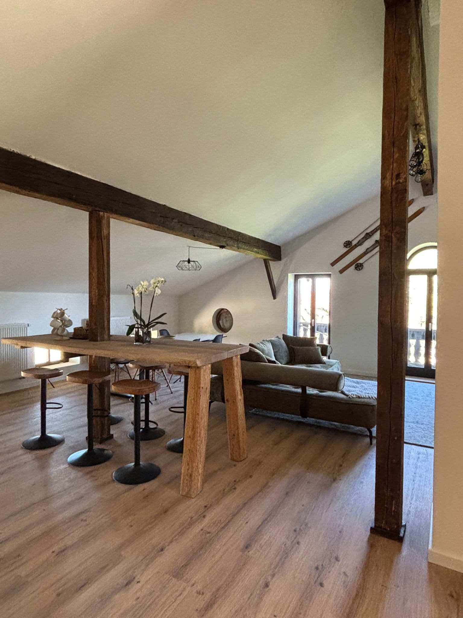 Rustic attic room with exposed beams, a large wooden table with stools, and green sofa.