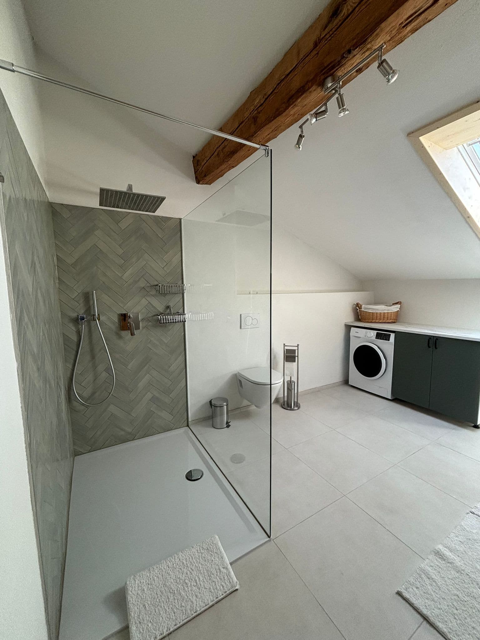 Modern attic bathroom with glass walk-in shower, grey herringbone tiles, and a laundry area.