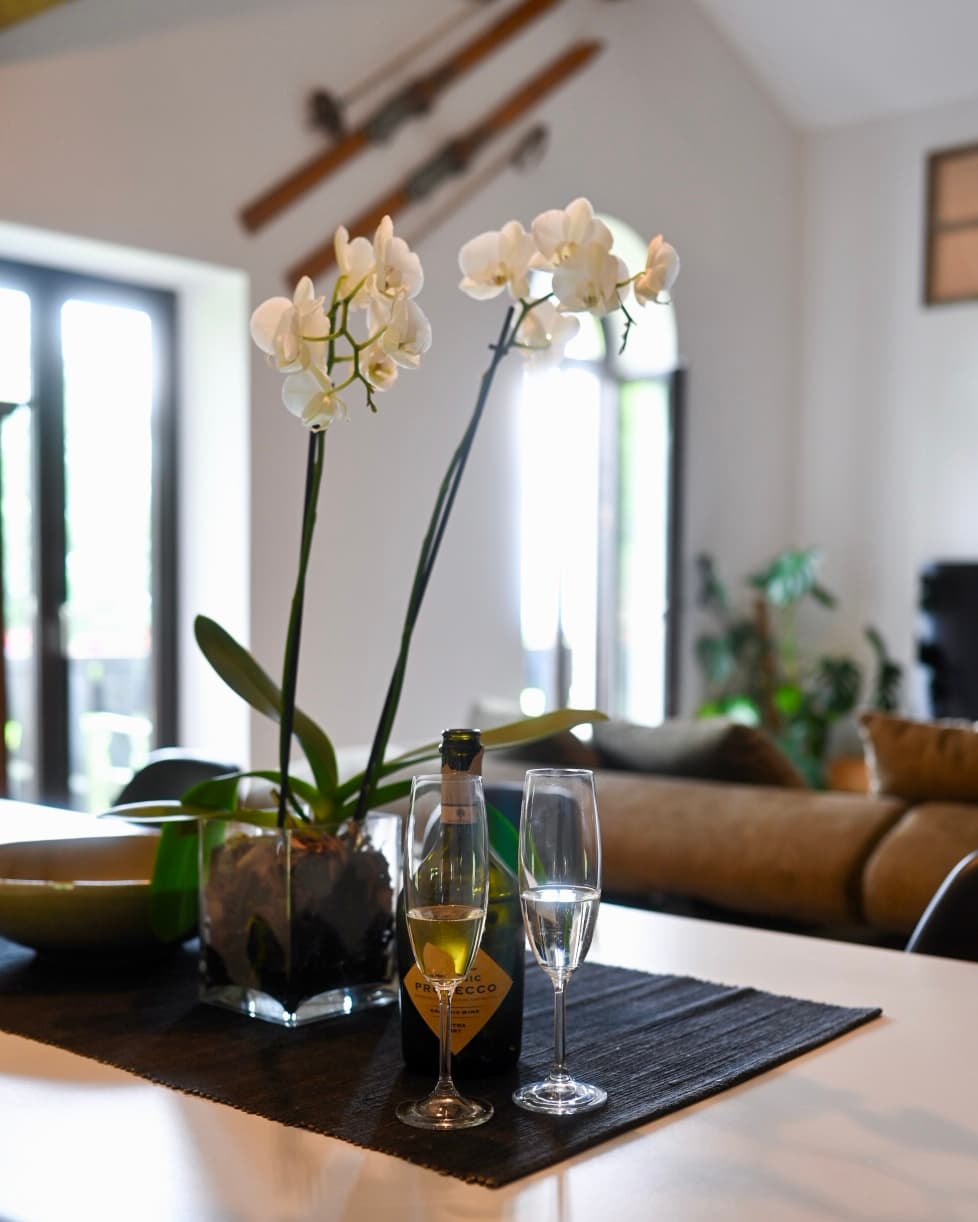 Two champagne flutes and a bottle of Prosecco next to a blooming white orchid.