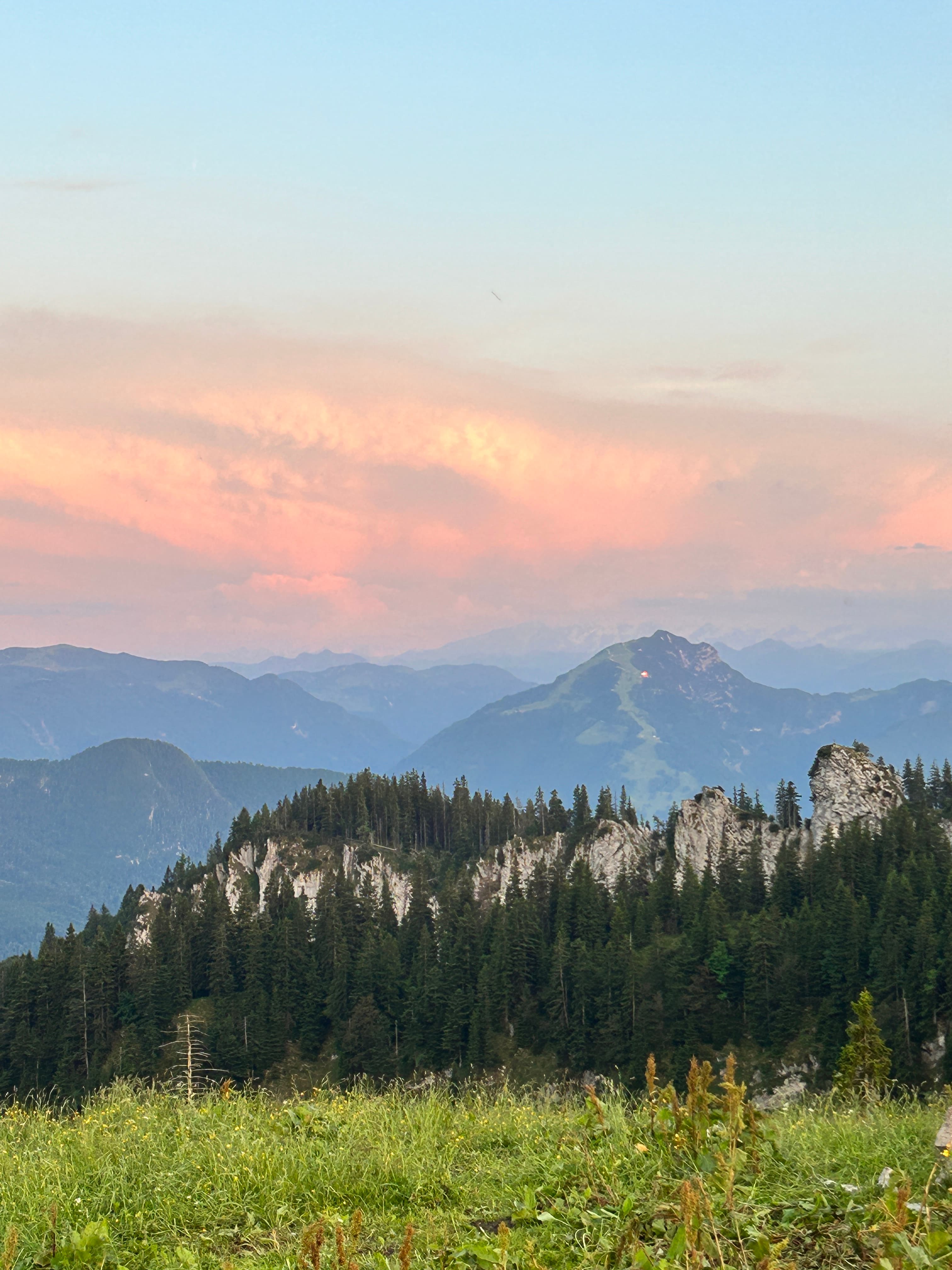 Evergreen forests and jagged white cliffs under a soft pink and orange sunset sky.