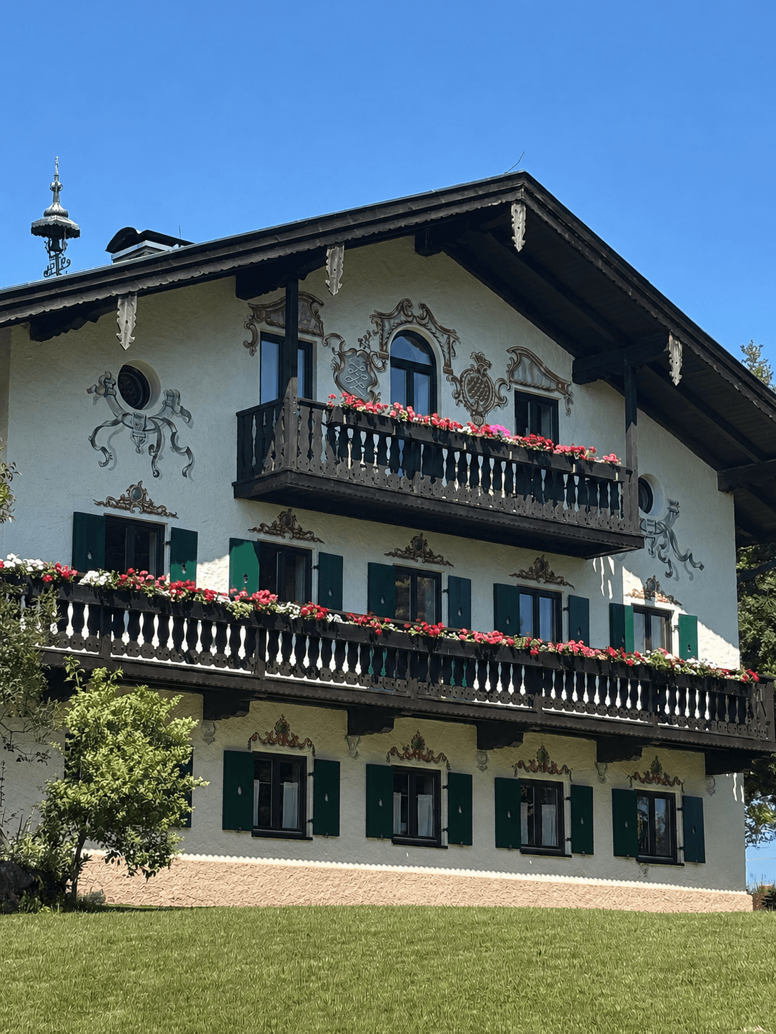 Traditional Alpine house with decorative wall paintings, green shutters, and flower-filled wooden balconies.