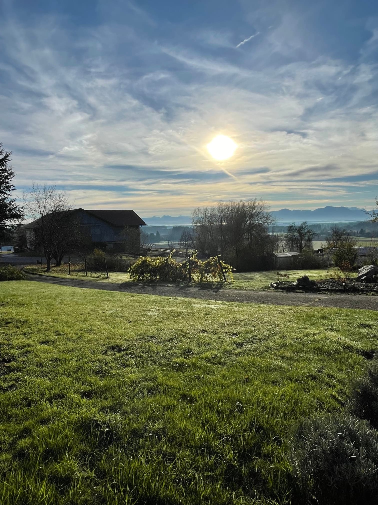 Sunlight glows over a green field, a rustic barn, and distant misty mountain peaks.