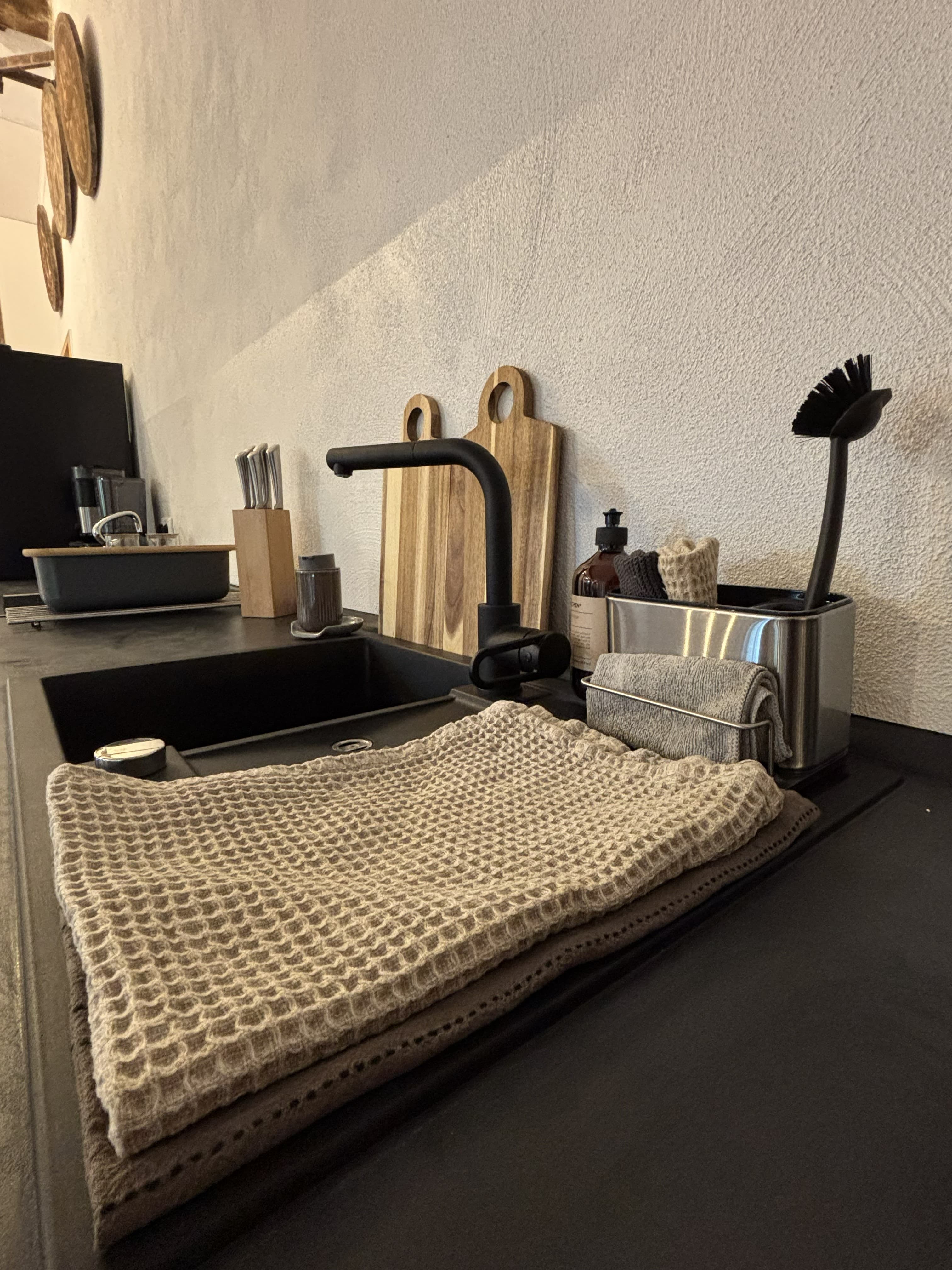 Modern black kitchen sink with matte faucet, wooden cutting boards, and a folded waffle-weave towel.