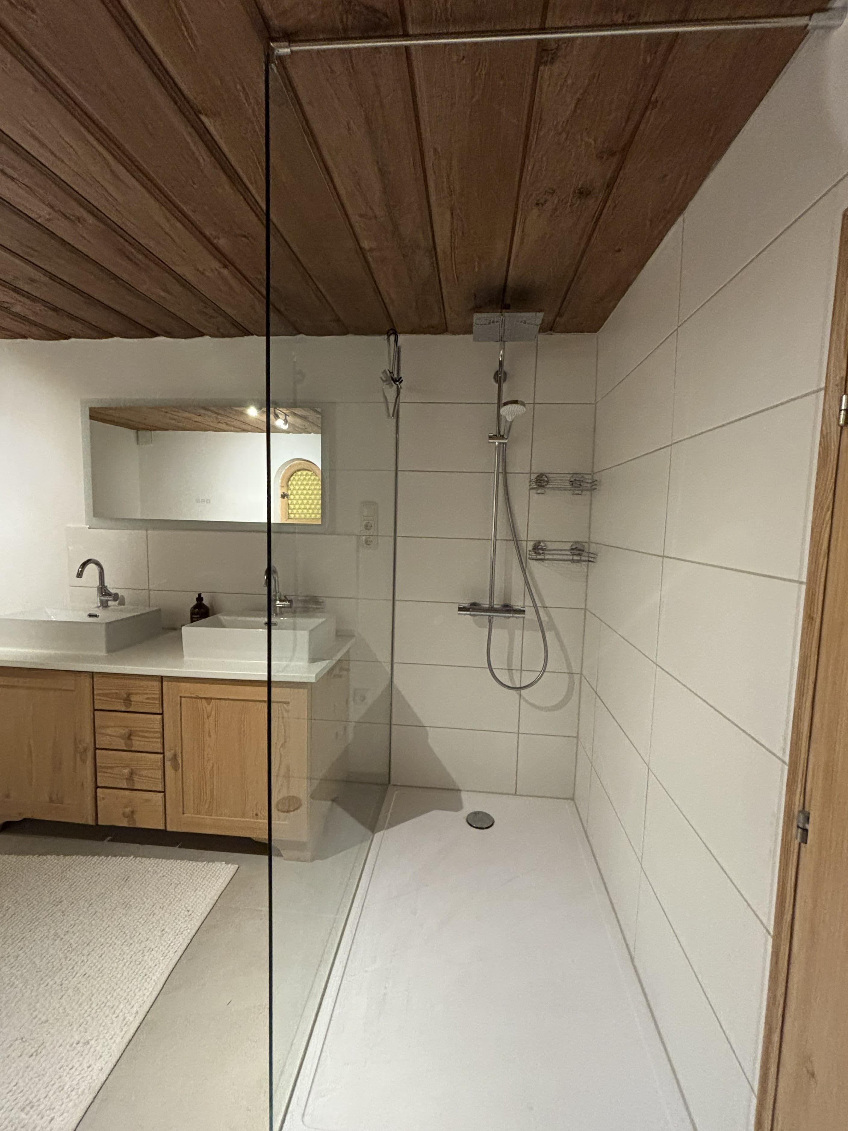 Modern bathroom with a glass walk-in shower, wooden plank ceiling, and double sink vanity.